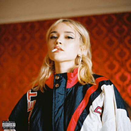 A blonde haired girl in a red room smoking a cigarette and wearing an oversized jacket